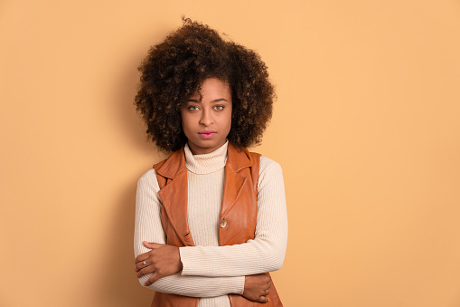 confident afro brazilian woman with arms crossed in beige studio background. portrait, real people concept.