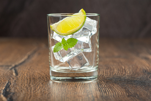 A glass with ice, mint leaves and a slice of lime on a dark wooden surface. Artificial ice cubes.