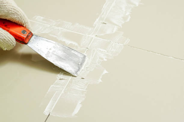istock Tiler laying the ceramic tile on the floor. Grouting ceramic tiles. Professional worker makes renovation. Construction. Hands of the tiler. Home renovation and building new house. 1629679042