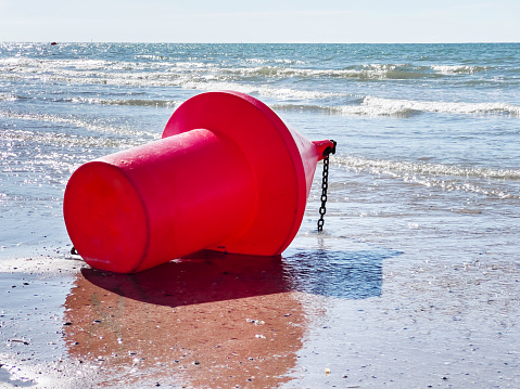 Red buoy attached with a metal chain on a sandy beach at low tide.