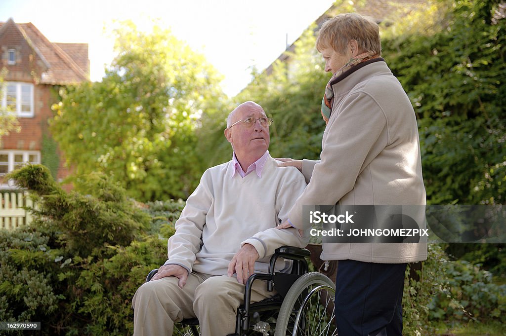 Coppia di anziani con sedia a rotelle - Foto stock royalty-free di Ambientazione esterna