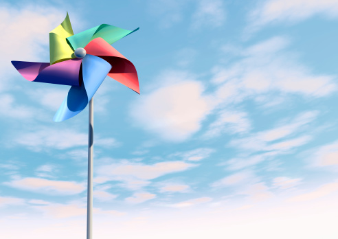 A regular toy pinwheel windmill with five differently colored vanes on a stick on a bluesky and cloud background