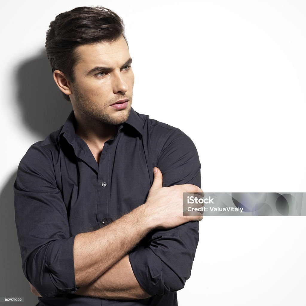 Fashion portrait of young man in black shirt Fashion portrait of young man in black shirt poses over wall with contrast shadows Hairstyle Stock Photo