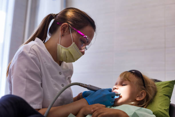 zubař ošetřuje zuby holčičky ve věku 5-6 let v zubní ordinaci na klinice. realistická fotografie zubaře lékaře s ošetřujícími zuby dítě dívka. koncepce stomatologie pro děti. kopírování reklamního textového prostoru - bolest zubů fotky - stock snímky, obrázky a fotky