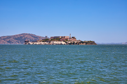 Image of Alcatraz Island on bright summer day with distant mountainous hill and choppy bay waters