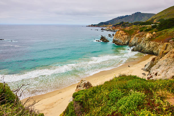 istock Beautiful scenic waves crashing against sandy beach with surrounding green covered cliffs 1629771097
