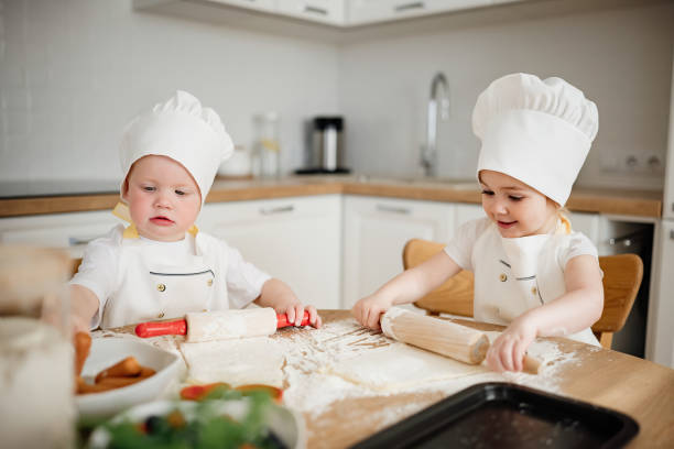 istock Adorable kids in chef hats and aprons rolling out pastry dough 1629778338