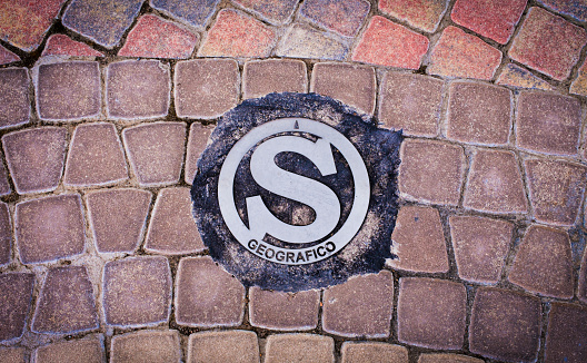 Zenith view of a letter S marking the geographic south, surrounded by a textured brick floor.