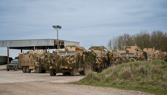 Salisbury, United Kingdom – March 08, 2023: close-up of several British army Mastiff protected patrol vehicles under green camouflage netting, Wiltshire UK