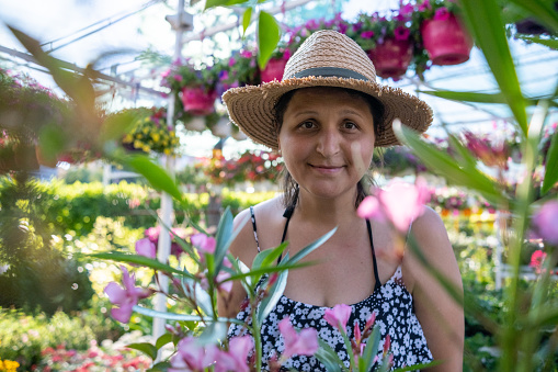 A young woman looks at flowers in a garden center. Multiple hanging flower pots with flowers in the background.