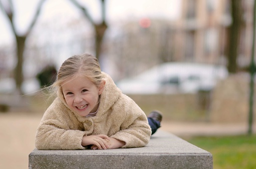 Selective focus of little laughing girl in city park lying on stone bench