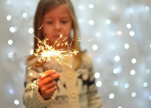 Selective focus of sparkler in little girl's hand with white bokeh of lights in background