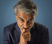 Angry senior businessman touching chin on blue background