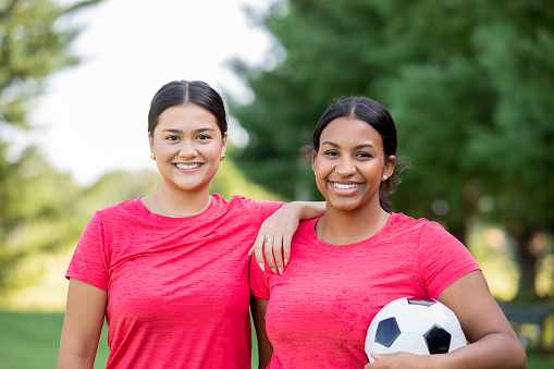 Young women playing soccer or football together outdoors on field and practicing for game
