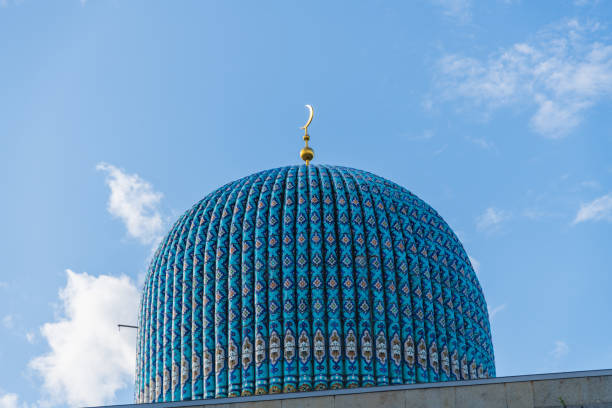 Close-up view of stone dome with blue roof and golden crescent of old Saint Petersburg Mosque against clear blue sky with white cloud. Religious architecture. Muslim culture theme.