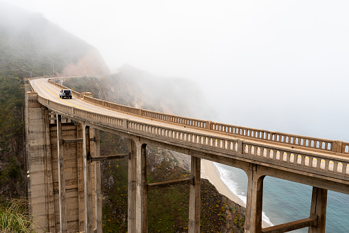 Panoramic view of a scenic fog raising above the bridge at Big Sur California by Pacific Coast Highway, Route 1, Bixby Creek Bridge, Rocky Creek Bridge. Magical landscape of California with moody colors of the morning