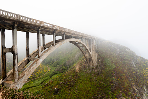 Scenic fog raising above the bridge at Big Sur California by Pacific Coast Highway, Route 1, Bixby Creek Bridge, Rocky Creek Bridge. Magical landscape of California with moody colors of the morning