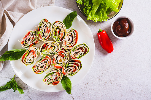 Italian rolled sandwiches with lettuce, ham and baked peppers in pita bread on a plate top view