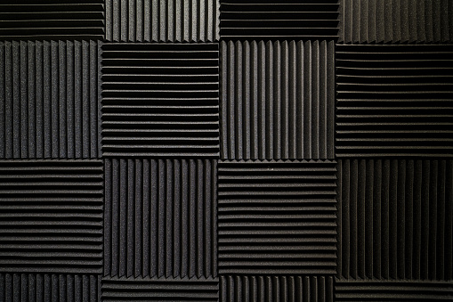 A pattern of black, square, soundproof foam blocks on a wall in an abstract background.