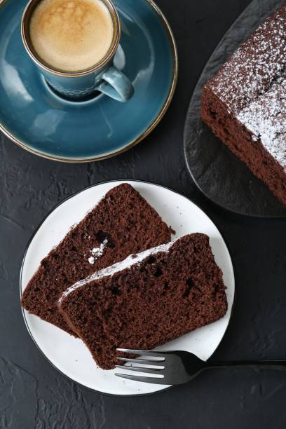 istock Tasty chocolate sponge cake with powdered sugar and coffee on black textured table, flat lay 1629904388