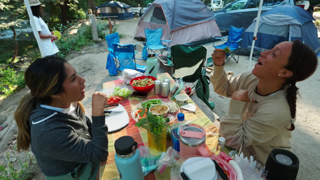 Two Friends Eating Snacks On a Table While Camping