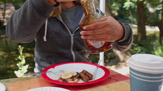 Female Camper Pouring Maple Syrup on Pancakes