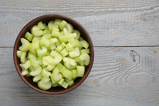 Fresh cut celery stalks in bowl on grey wooden table, top view. Space for text