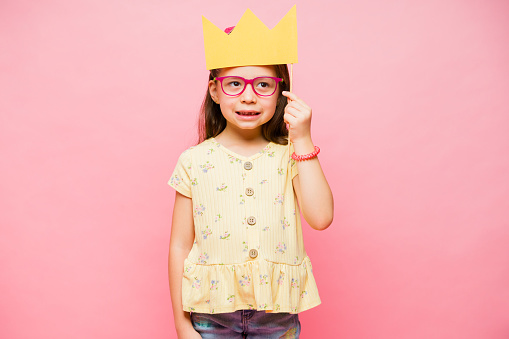 Beautiful little girl wearing a princess crown playing fun games and smiling against a pink background