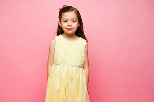 Adorable happy little girl smiling wearing a cute yellow dress looking happy in front of a pink studio background