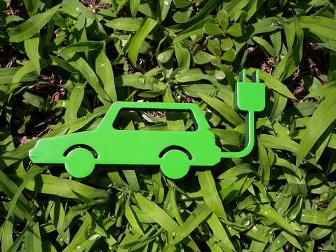 The figurine of the electric car lies on the green grass. Sustainability concept.
