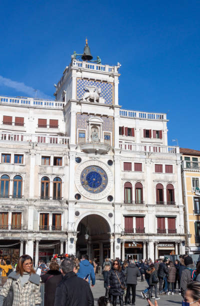 Venice, Italy - February 13, 2022: Clock tower in San Macro square in sunny day with many people.