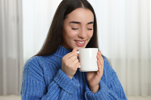 Happy young woman holding white ceramic mug at home