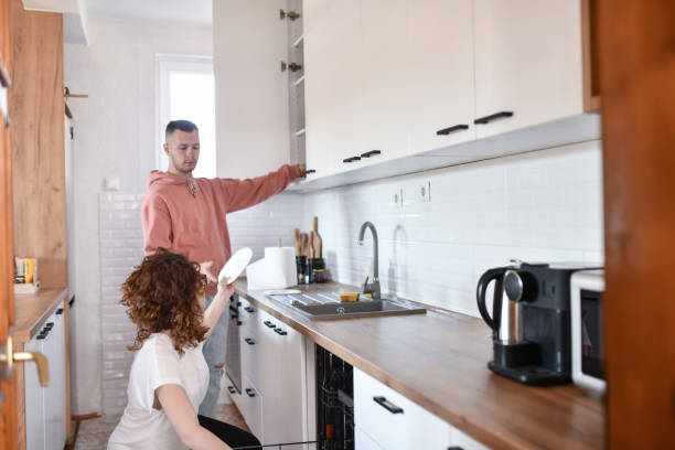 istock Beautiful Curly Female Passing Dishes To Husband While Both Work Together On House Chores 1630049793