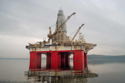Oil drilling rig floating on water. Gray cloudy sky and calm sea surface