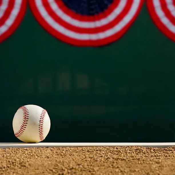 A baseball sitting on the pitcher mound's rubber with the center field fence in the background decorated for the World Series.