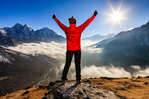 Young woman, wearing red jacket, lifts her arms in victory. She is standing on the top of a mountain and watching sunset over Himalayas .Mount Everest National Park. This is the highest national park in the world, with the entire park located above 3,000 m ( 9,700 ft). This park includes three peaks higher than 8,000 m, including Mt Everest. Therefore, most of the park area is very rugged and steep, with its terrain cut by deep rivers and glaciers. Unlike other parks in the plain areas, this park can be divided into four climate zones because of the rising altitude.