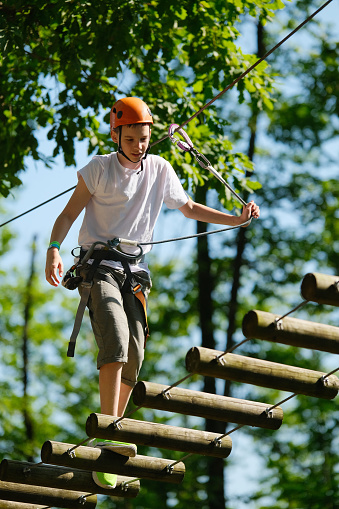 Portrait of teenage boy having fun at outdoor extreme adventure rope park. Active childhood, healthy lifestyle, playing outdoors, children in nature.