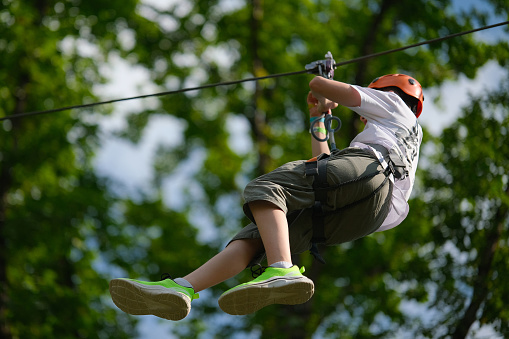 Teenage boy on zipline having fun at outdoor extreme adventure park. Active childhood, healthy lifestyle, playing outdoors, children in nature.