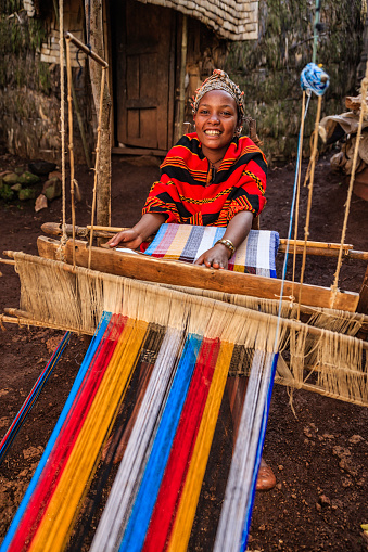 Young African woman from Dorze tribe weaving colorful traditional scarf in the village close to Arba Minch town, southern Ethiopia, Africa.