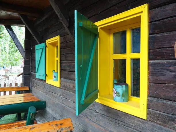 Ethno-folk wooden shutters on a window with a wooden frame, painted green and yellow. Vintage Serbian house, exterior. Architectural complex Stanisici, Bielina, Bosnia and Herzegovina. Log cabin