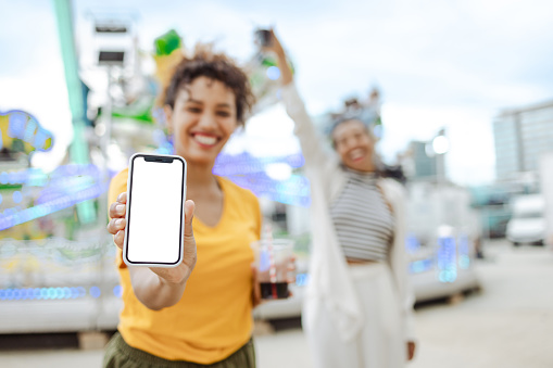 Cheerful women holding a mobile phone with a white screen while partying at the Carnival