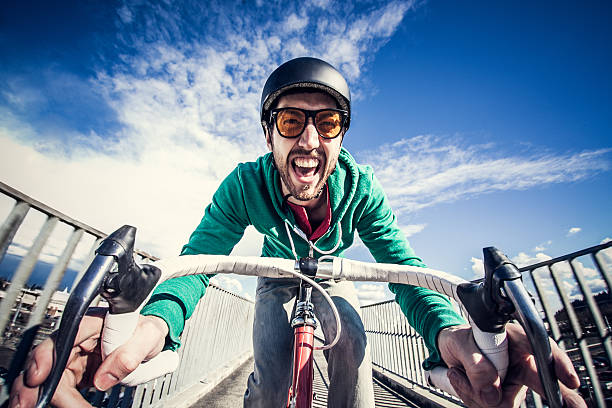 A young hipster looking man on a red racing street bicycle rides on a pedestrian overpass in a Portland city neighborhood.  He laughs / shouts with excitement, a broad smile on his face.  Horizontal with copy space.