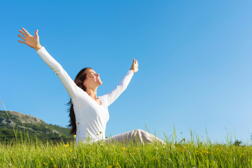 Pretty young woman with arms raised enjoying beautiful day in the nature.