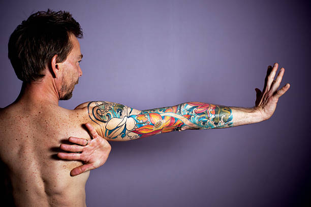tattoo portrait mid adult man holding his arm aloft with fingers on hands as to make a stop gesture and head and face in profile.  horizontal composition.  his left hand is wrapped underneath in armpit with wedding band on ring finger. forearm tattoos men stock pictures, royalty-free photos & images