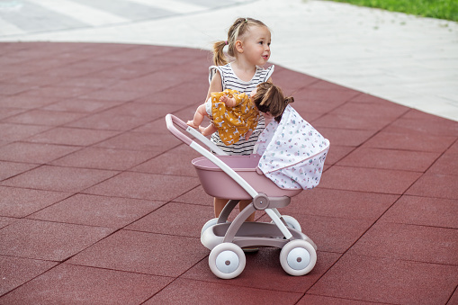 Little girl with doll in stroller. Copy space. Two years old. Developmental milestones. Early years