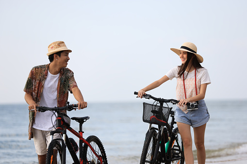 A happy young couple  walking on a bicycle and looking at each other on the beach  against a clear sky on a sunny day