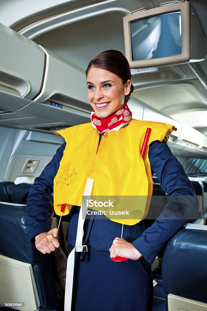 Airline safety demonstration Beautiful flight attendant standing in an airplane and demonstrating a life jacket before taking off. Cabin Crew Stock Photo