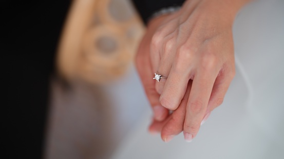 A close-up photo of a bride and a groom holding each other's hands.