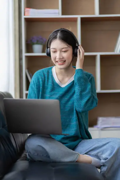 Photo of Beautiful young Asian woman in casual clothes Use a laptop and smile while sitting on the couch. work from home Work remotely, surf the net, New Normal concept