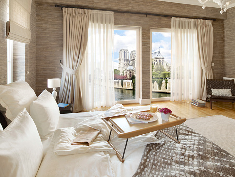 Wide angle shot of a comfortable bedroom and breakfast tray with image montaged Notre Dame Cathedral in Paris